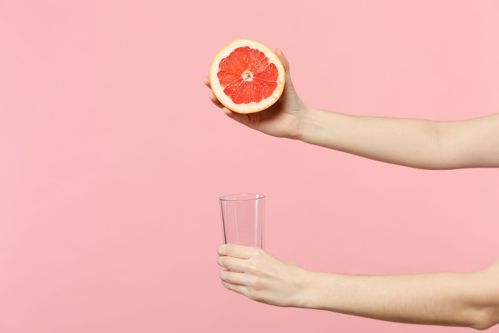 Hand holding a sliced-open grapefruit above drinking glass before squeezing