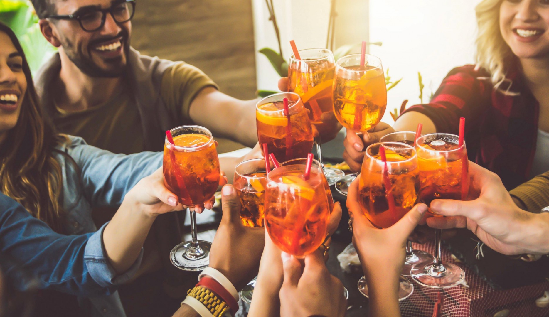 close-up of a group of friends raising their cocktail glasses in the air for a toast